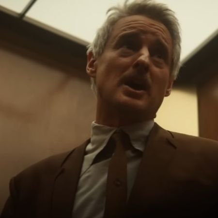 Owen Wilson is wearing a brown suit and is in an elevator.